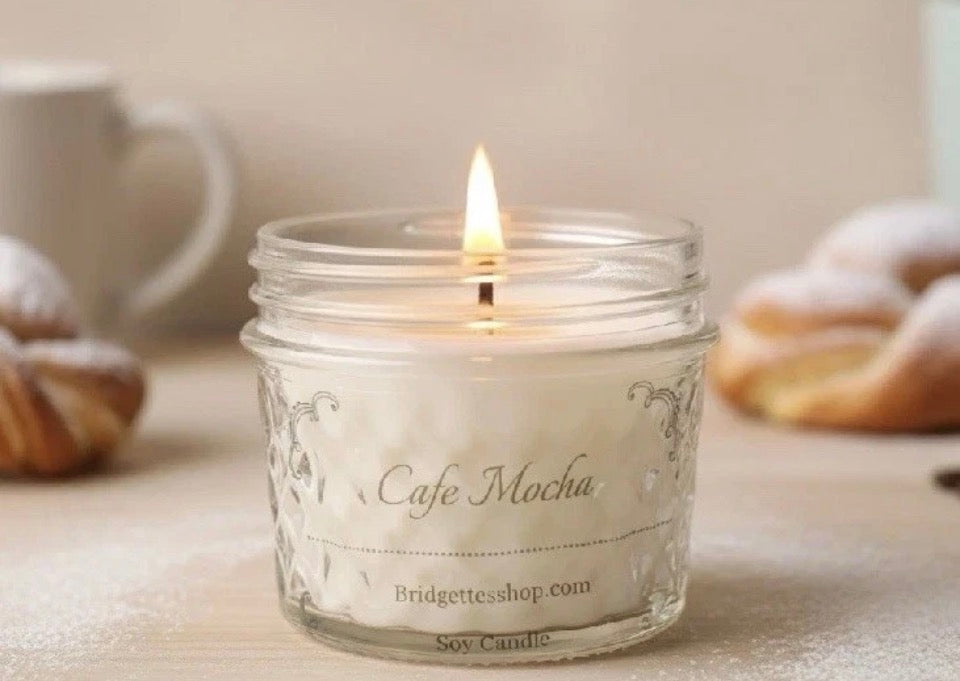 Candle in a jar labeled 'Cafe Mocha' with a blurred background of pastries and a mug.