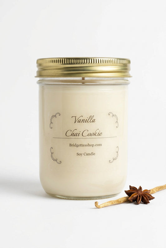 A glass jar candle with a gold metal lid and cream-colored wax, labeled 'Vanilla Chai Cookie' by Bridgetteshop.com.