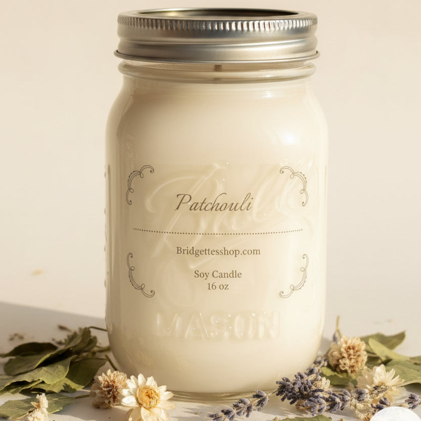 White candle in a mason jar with 'Patchouli' branding on a wooden surface