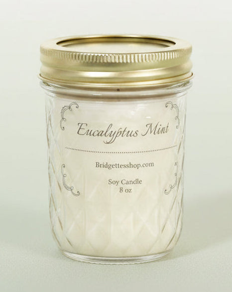 Glass candle jar with gold lid labeled 'Eucalyptus Mint' on a light background