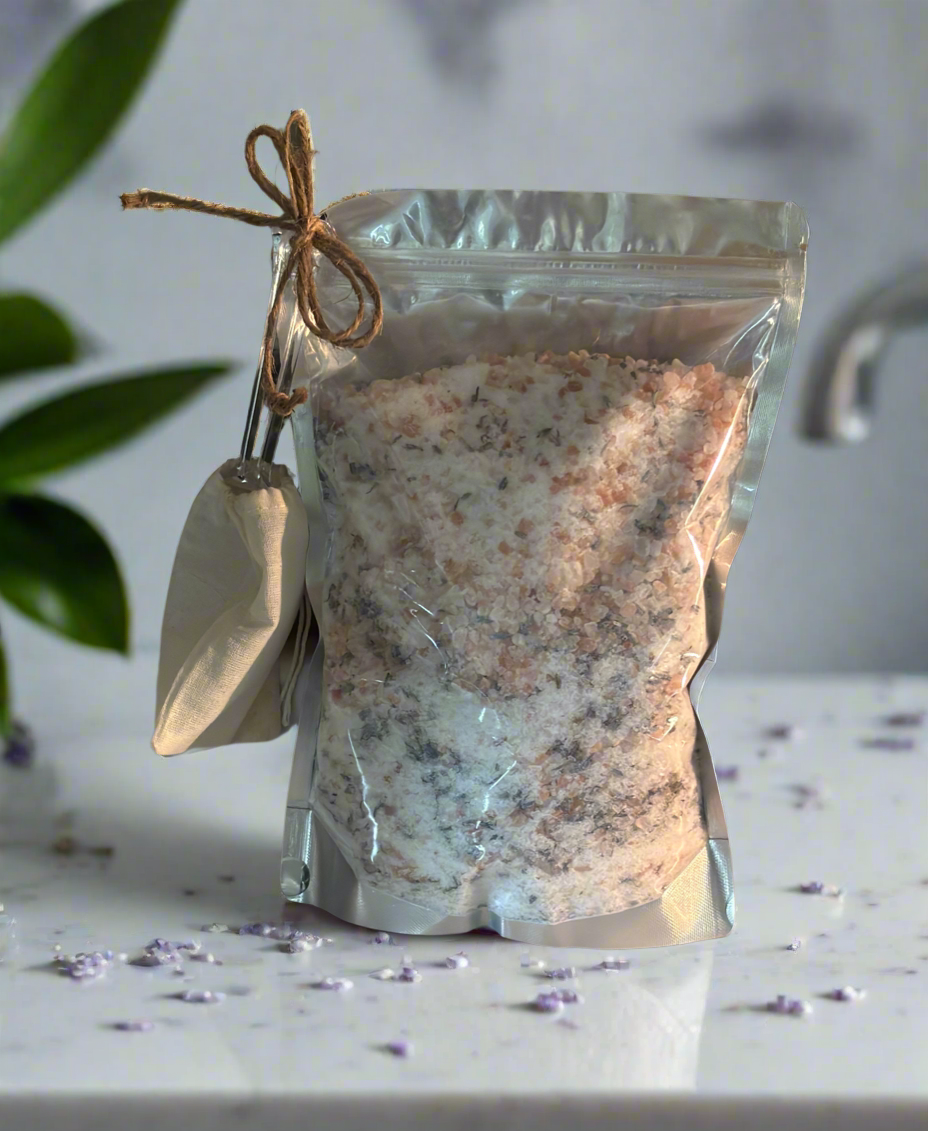 Bag of bath salts with a scoop on a marble surface, with a plant in the background.