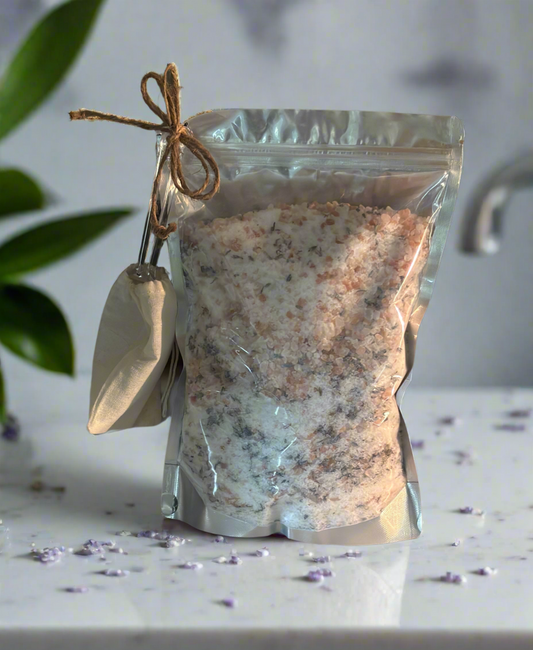 Bag of bath salts with a scoop on a marble surface, with a plant in the background.