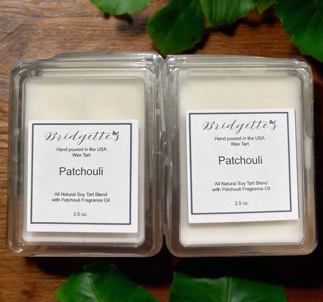 Two Bridgette's Patchouli wax tarts in packaging on a wooden surface with green leaves.