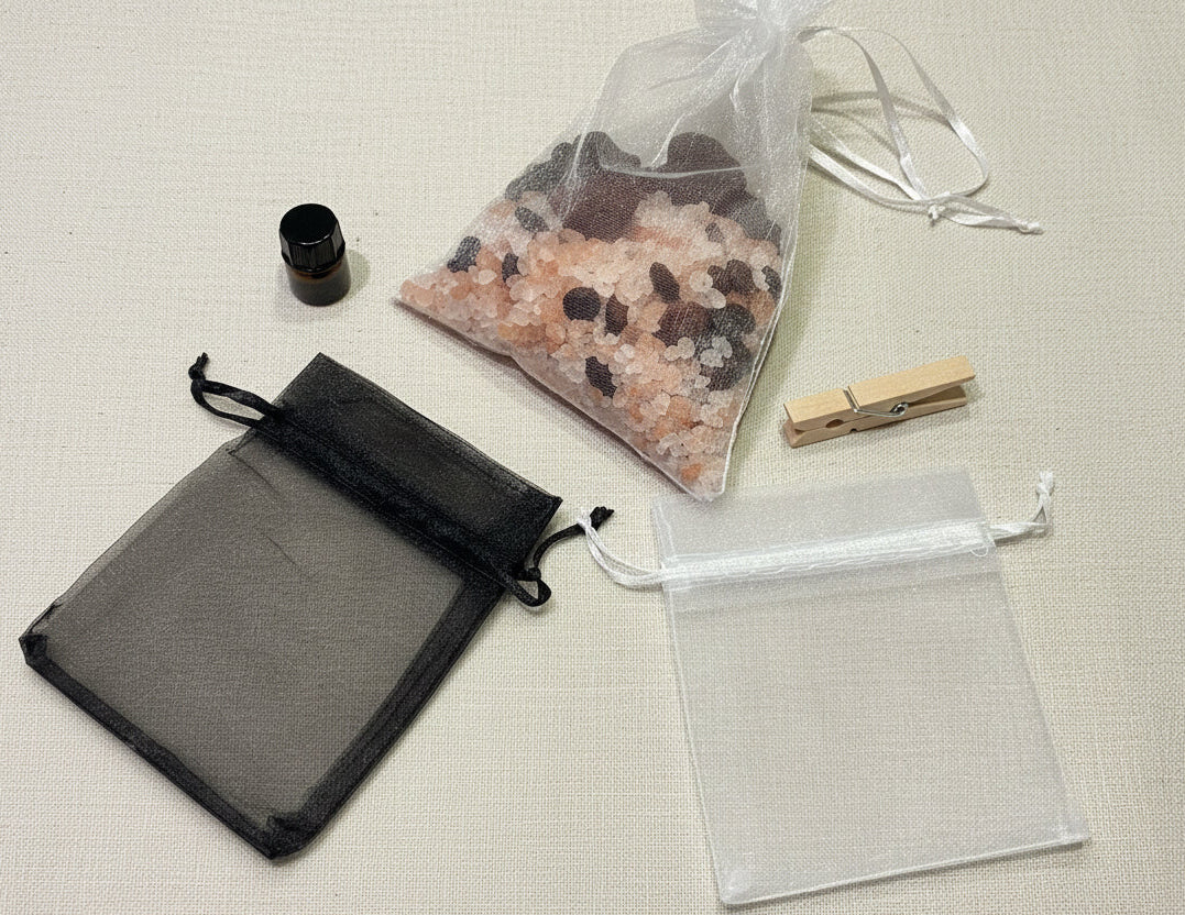 Black drawstring bag, clear organza bag, and small container on a wooden surface