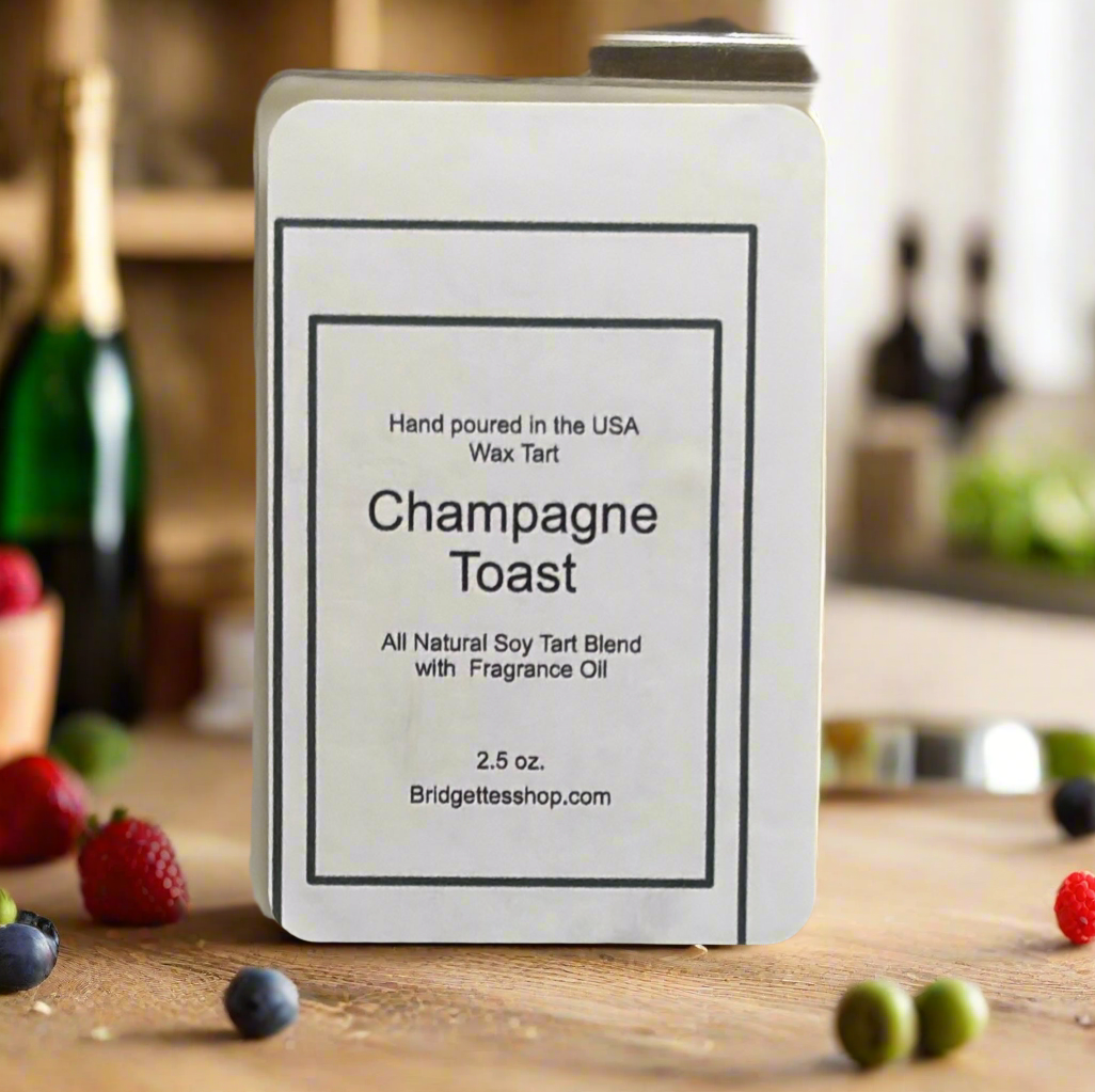 Wax tart container labeled 'Champagne Toast' on a wooden surface with fruits and bottles in the background.