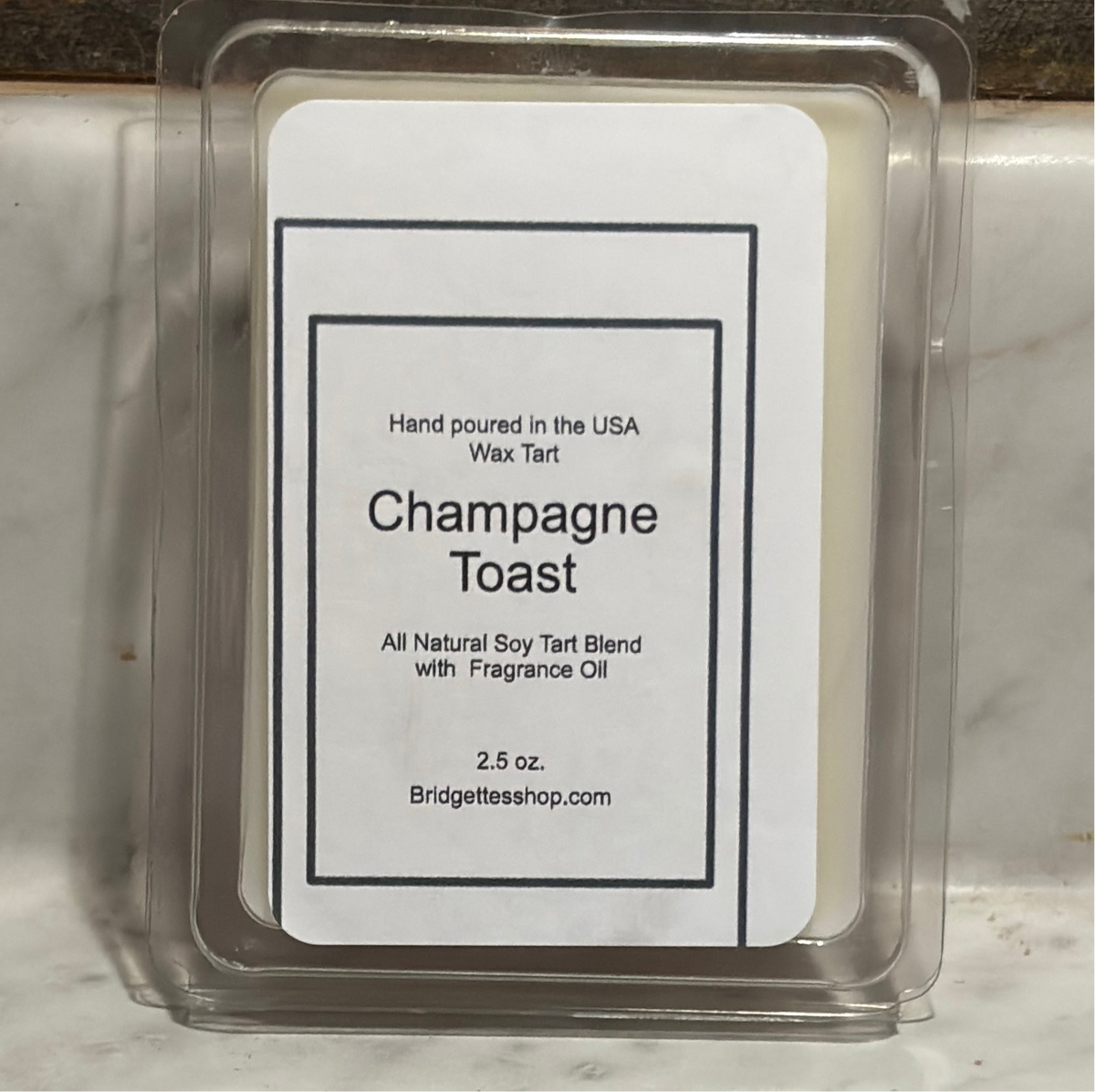 Wax tart labeled 'Champagne Toast' with a Bridgettesshop.com label on a marble surface.