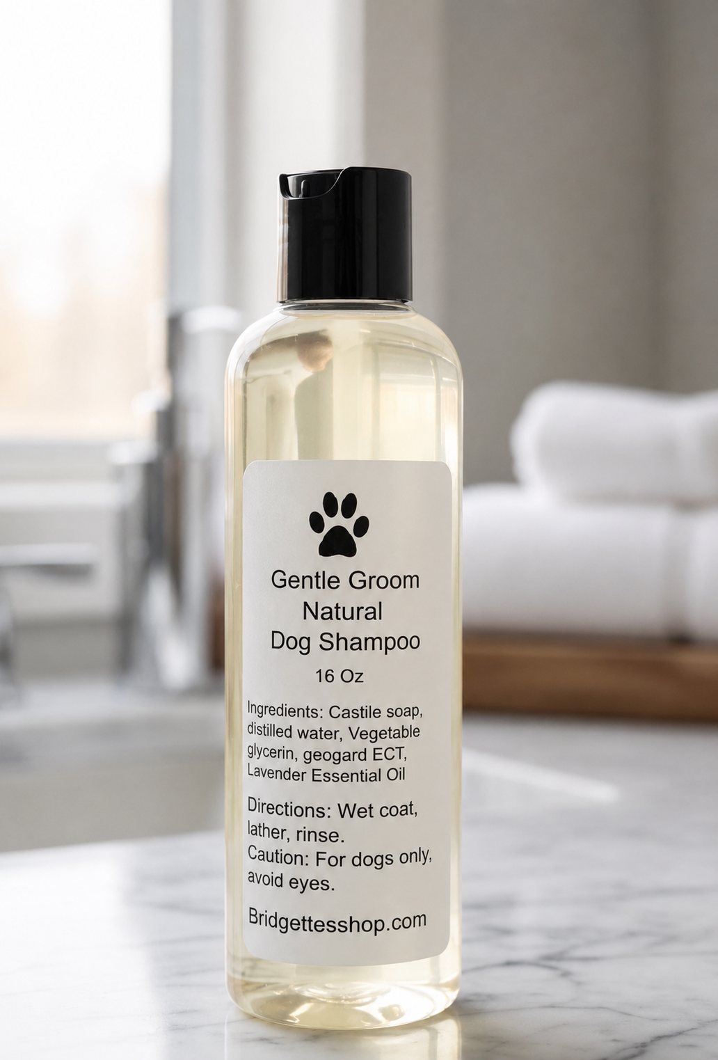 A 16 oz bottle of Bridgettesshop.com Gentle Groom Natural Dog Shampoo, featuring a clear plastic bottle with a black cap and a white label, set on a marble countertop with a blurred bathroom background.