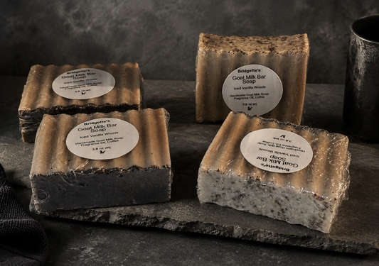 Four goat milk soap bars with visible branding on a dark surface