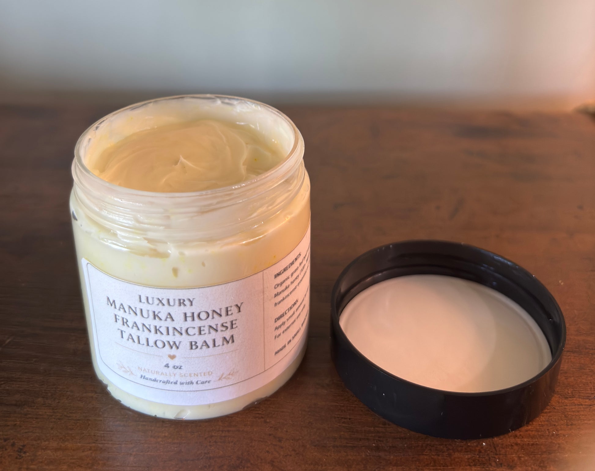 Manuka Honey Frankincense Tallow Balm jar with open lid on a wooden surface
